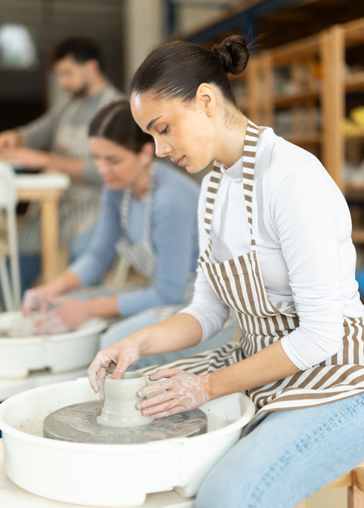 Two girls craftspersons busy molding clay products on pottery wheel
