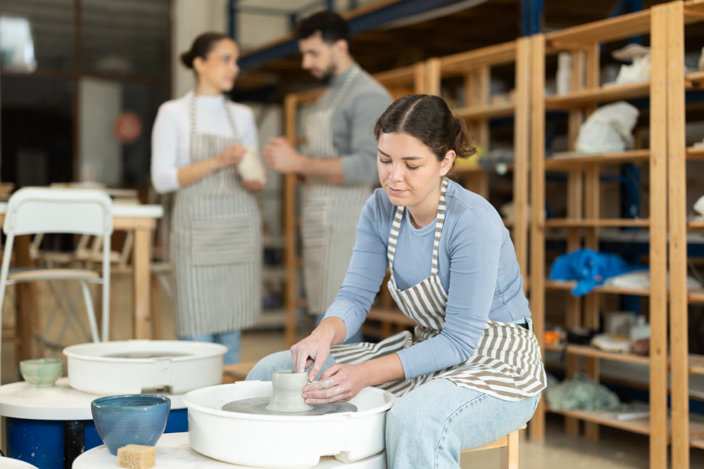 Girl craftspersons busy molding clay products on pottery wheel