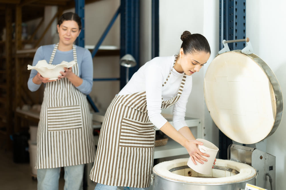 Girl in apron put or takes clay vase out of oven