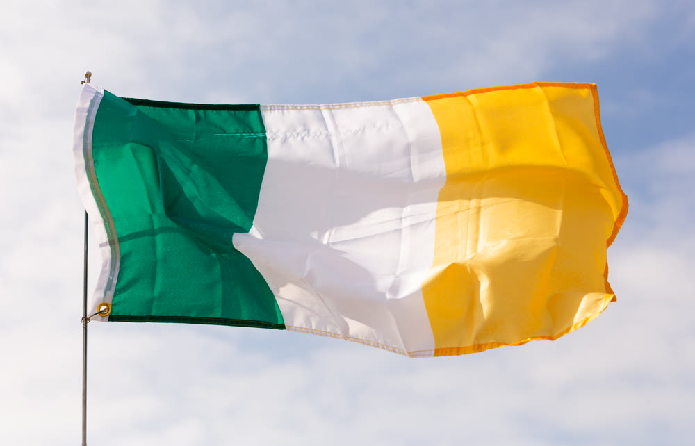 Flag of Ireland waving on flagstaff against blue sky