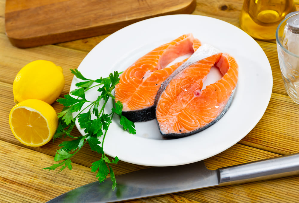 Plate with raw salmon slices, fresh parsley, garlic and lemon