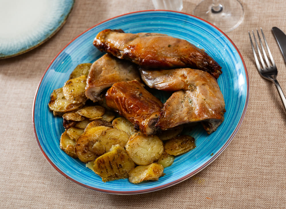 Lunch is served on plate - pieces of young rabbit baked with slice of potato. Close-up