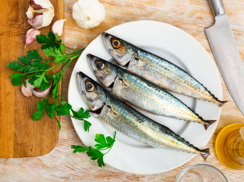 Whole mackerel carcasses, parsley, garlic are on wooden background