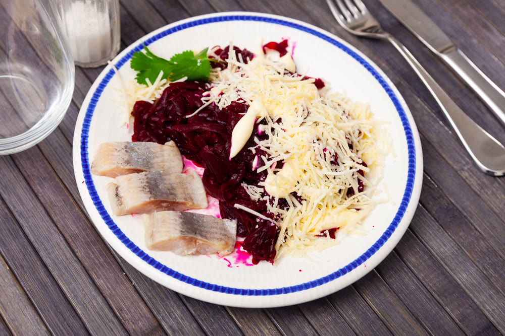 Sliced herring with grated beetroot and cheese served on table