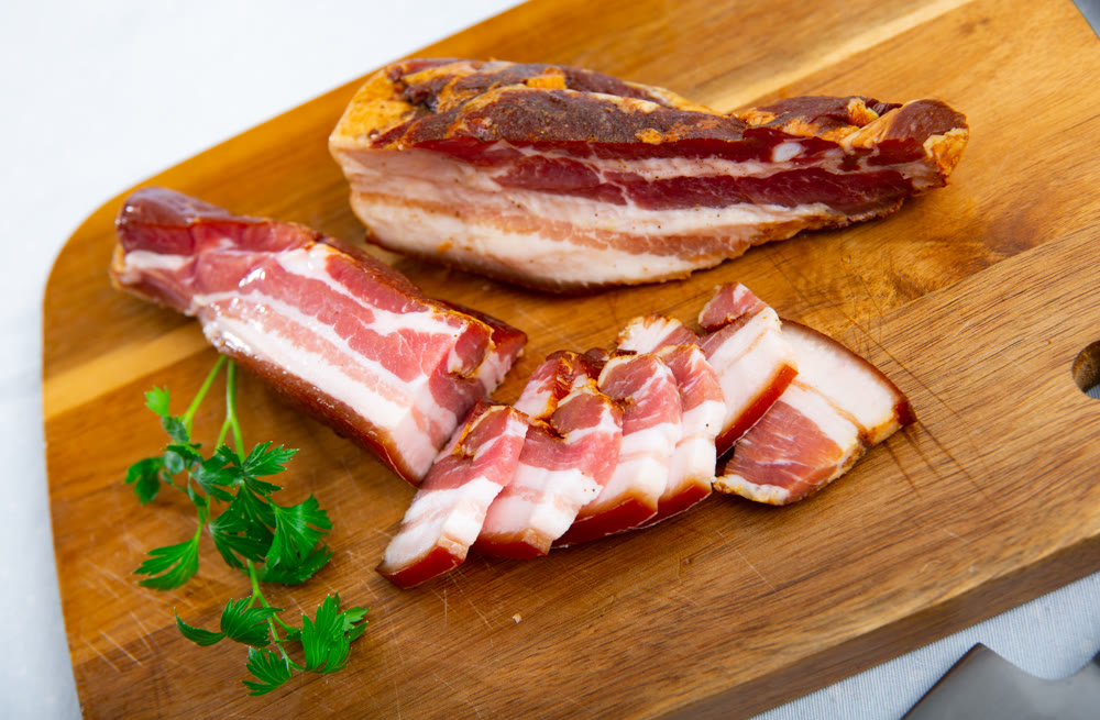 Sliced smoked pork belly bacon and greens on wooden board