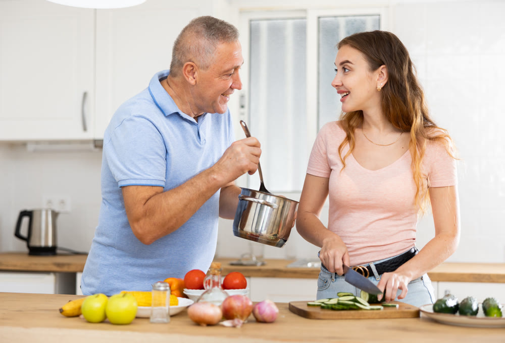 Adult daughter cooks dinner in kitchen with an elderly father