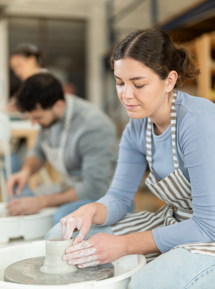 Woman in ceramics workshop with pottery wheel and various clay vessels