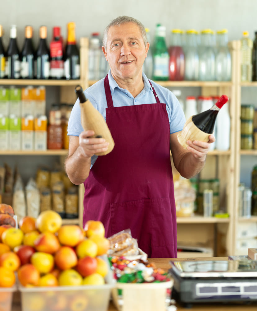 Senior man offers to buy alcohol, holds out bottles towards buyer, demonstrates best offers.