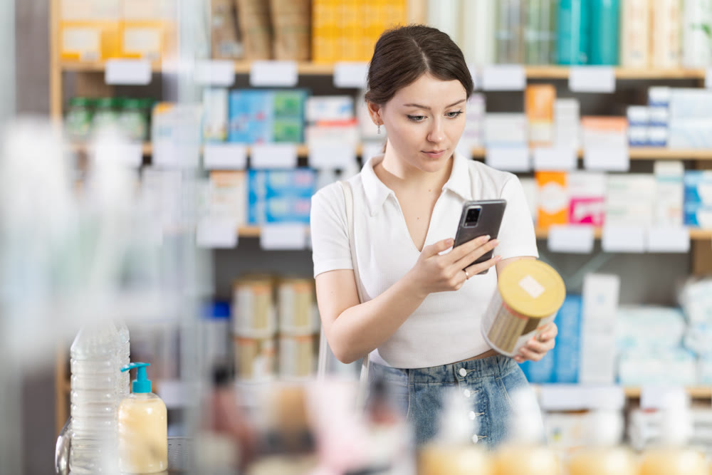 Woman checking baby formula ingredients with phone at pharmacy