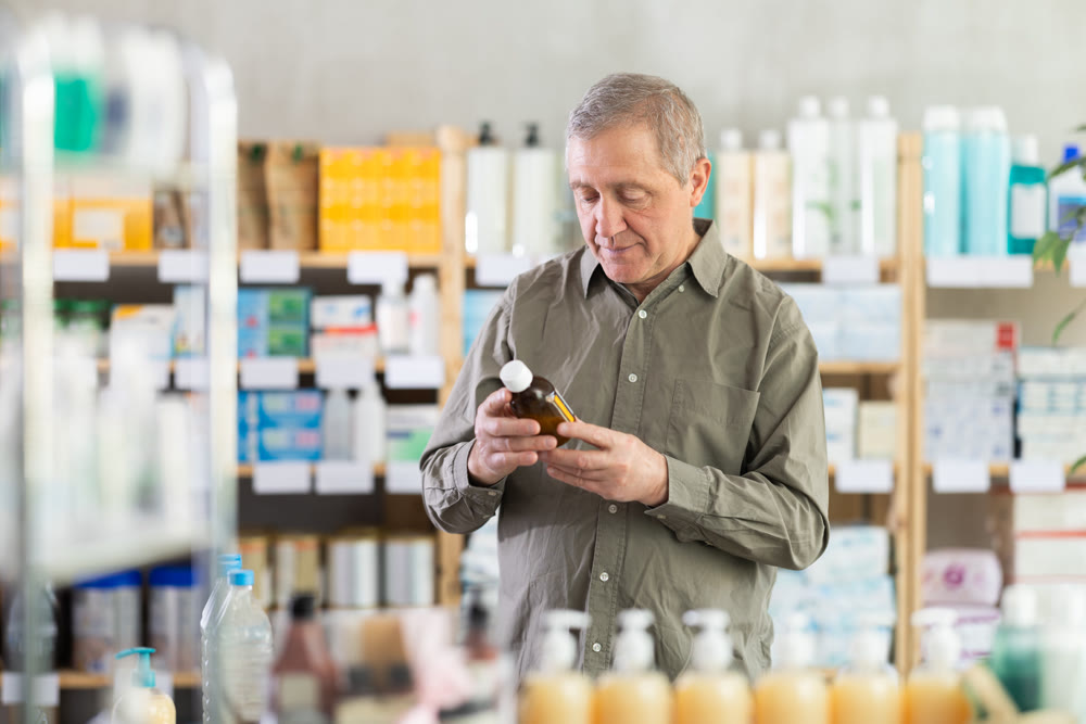 Elderly man examining bottle of fever-reducing syrup in pharmacy