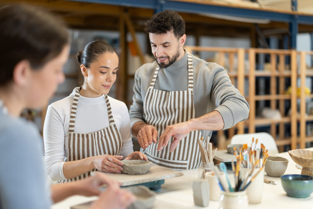 Male master leaned over to girl and helps to sculpting from clay