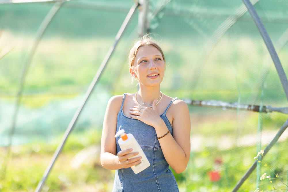 Young woman applying sunscreen in garden greenhouse