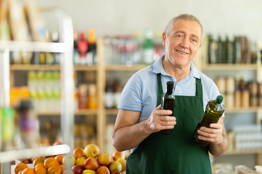 Senior man offers to buy vegetable oil, holds out bottles towards buyer, demonstrates best offers.