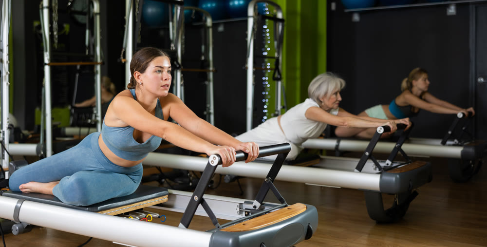 Girl sitting on foldable bed reformer performs exercises, strengthening body and muscles