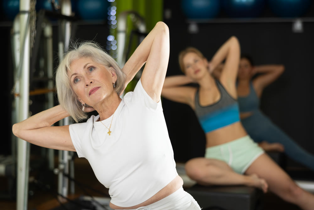 Gray-haired woman sitting on a Pilates platform