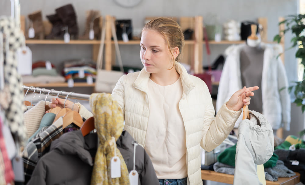 Attentive teenage girl choosing lightweight jacket in clothing store