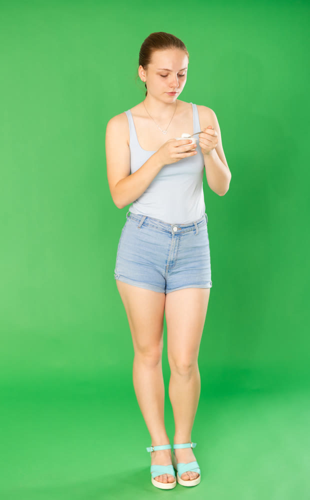 Teenage girl eating yogurt in front of green screen
