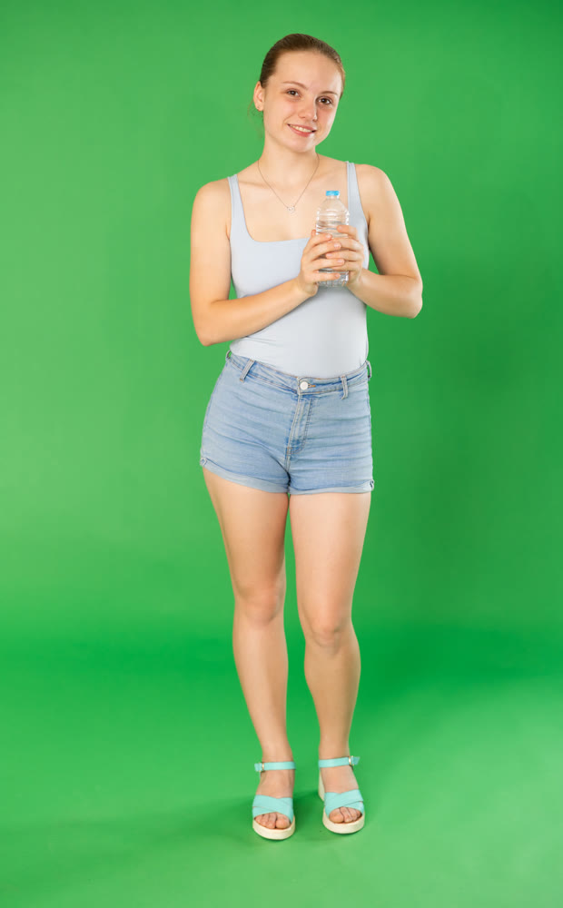 Teenage girl drinking water in front of green screen