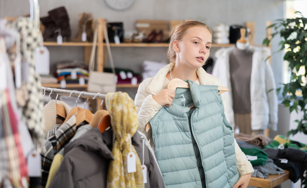 While shopping, teen girl browsing goods items and choose elect down vest in store