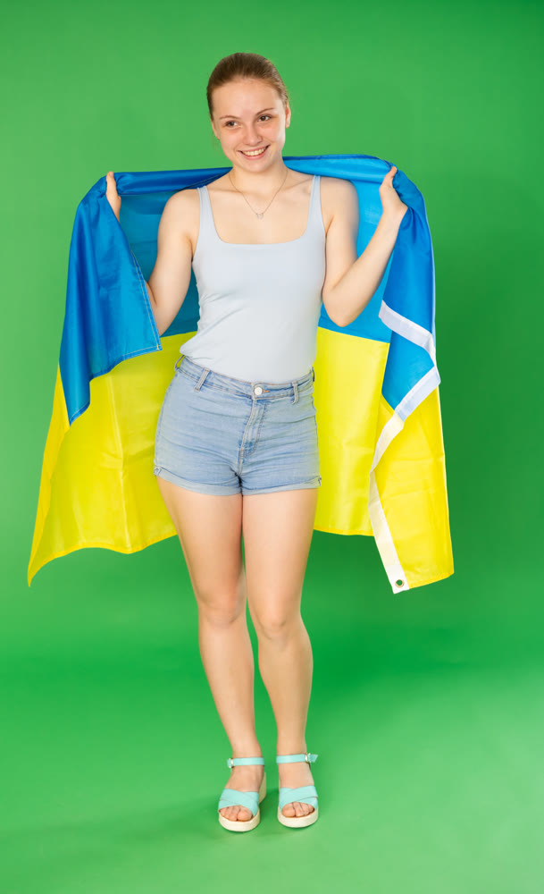 Teenage girl in blue top with large flag of Ukraine posing on green background. Chroma key compositing