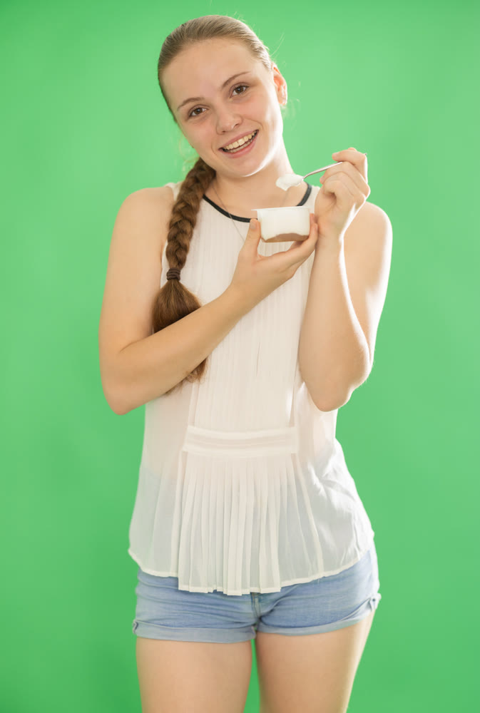 Girl in white blouse eats yogurt. Chroma key compositing