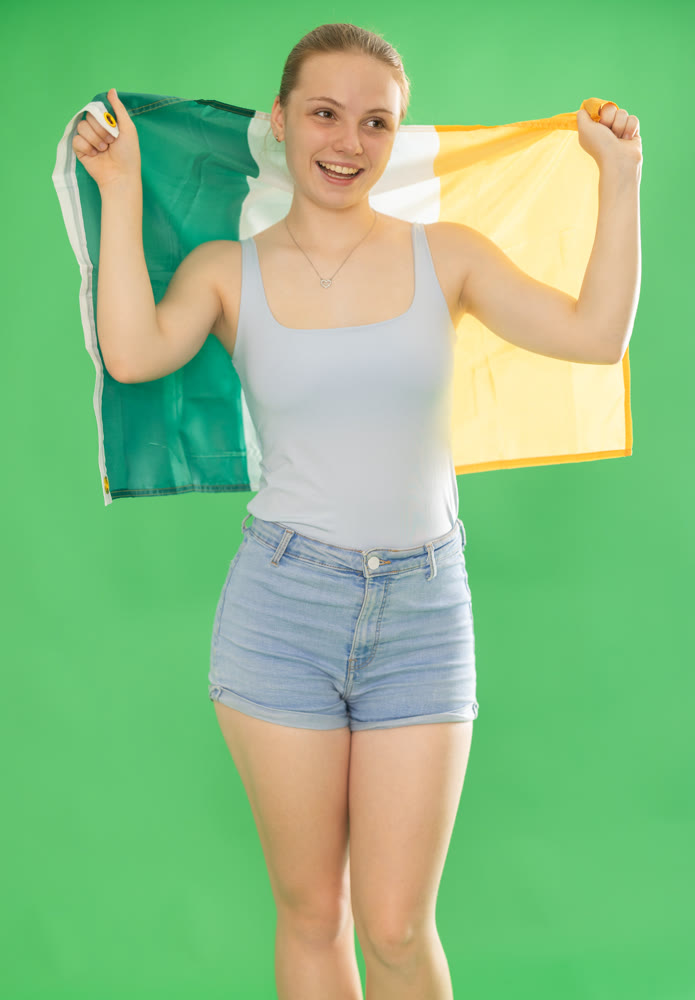 woman in casual clothes holds the flag of Ireland against a background of chroma key