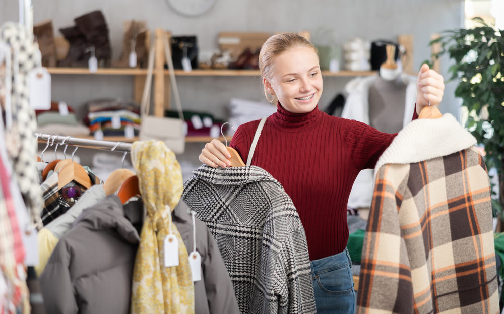 Positive teen girl choosing winter coat in clothing store