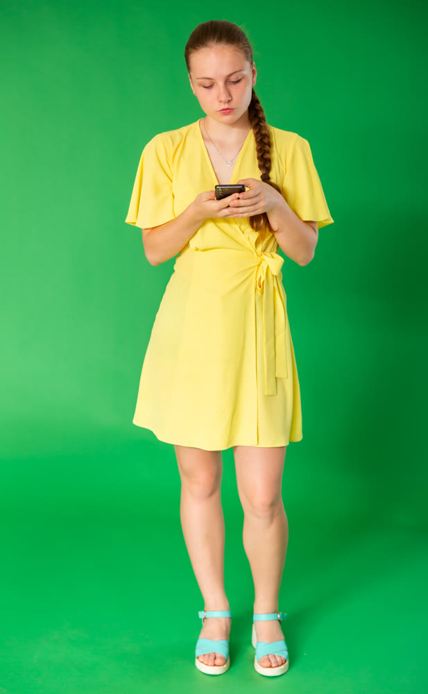 Teenage girl scrolling smartphone in front of green screen