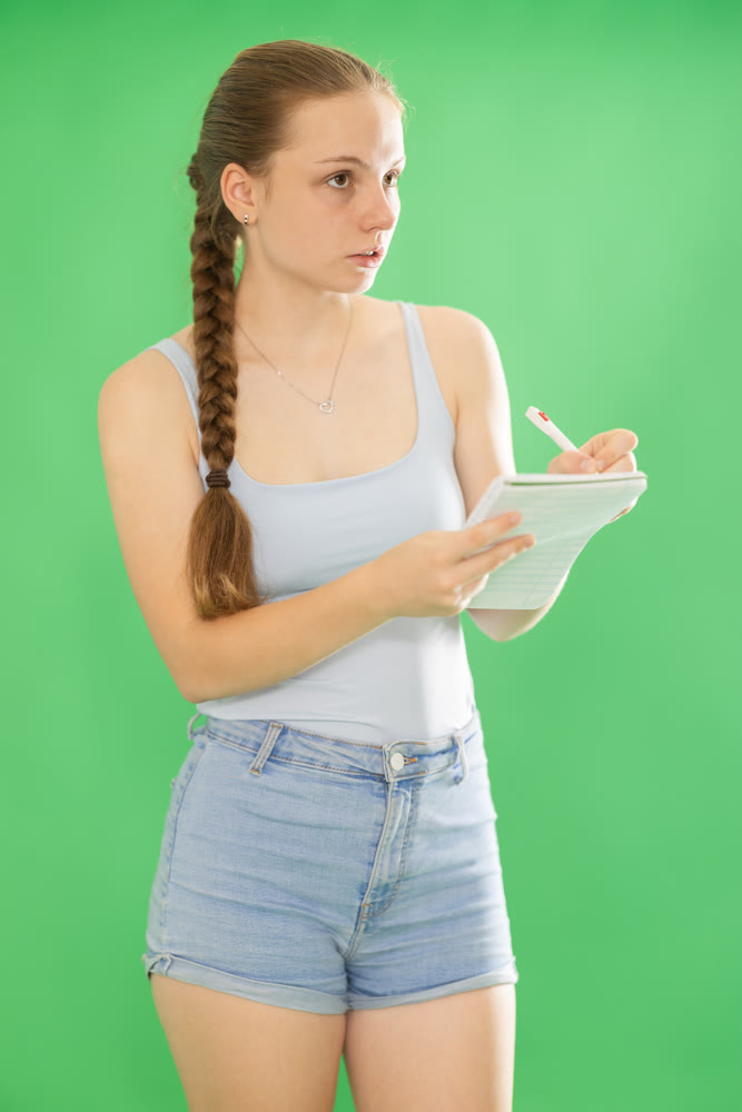 Teenage girl in blue top takes notes in notebook on green background. Chroma key compositing