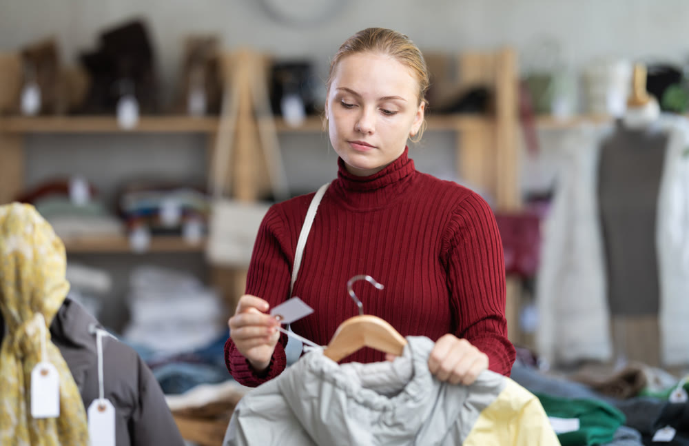 Attentive teenage girl choosing lightweight jacket in clothing store