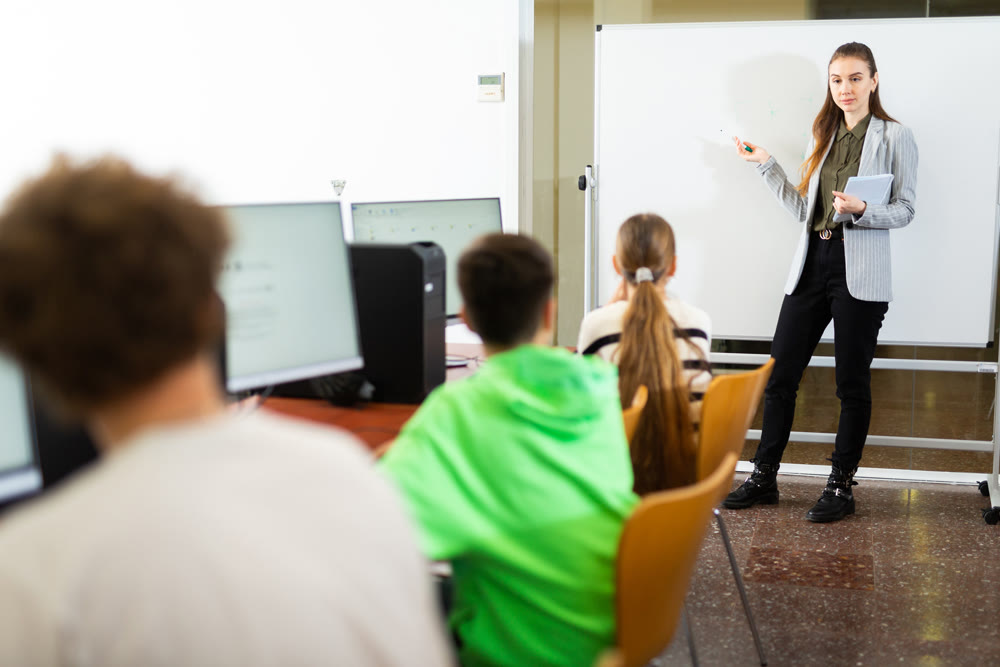 Female teacher standing at whiteboard during lesson in computer class