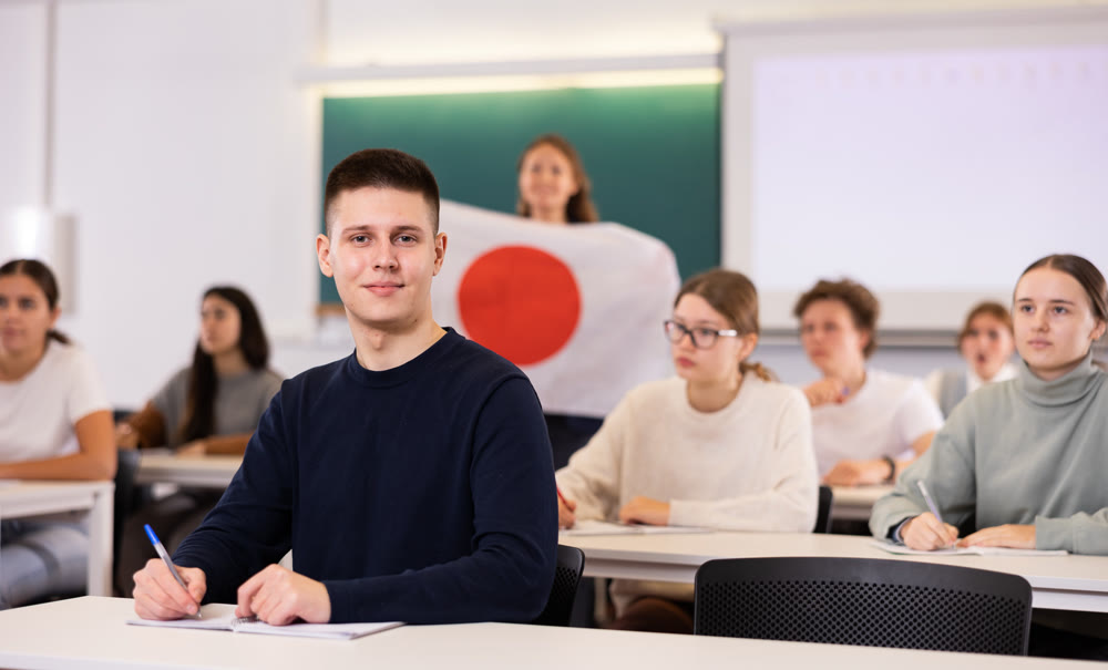 Teacher stands behind students with flag of Japan