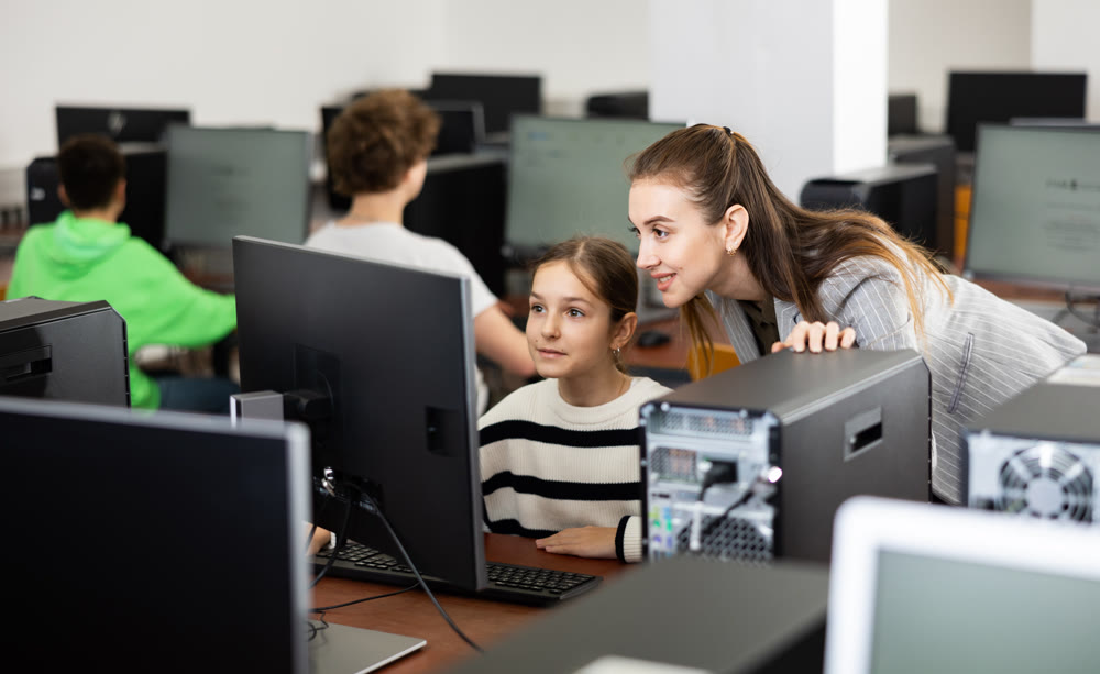 Positive woman teacher together with the girl teaches how to work on computer
