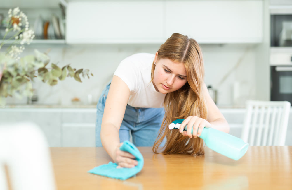 in kitchen,positive housewife in casual clothes holds rag in hands and cleans surface of table