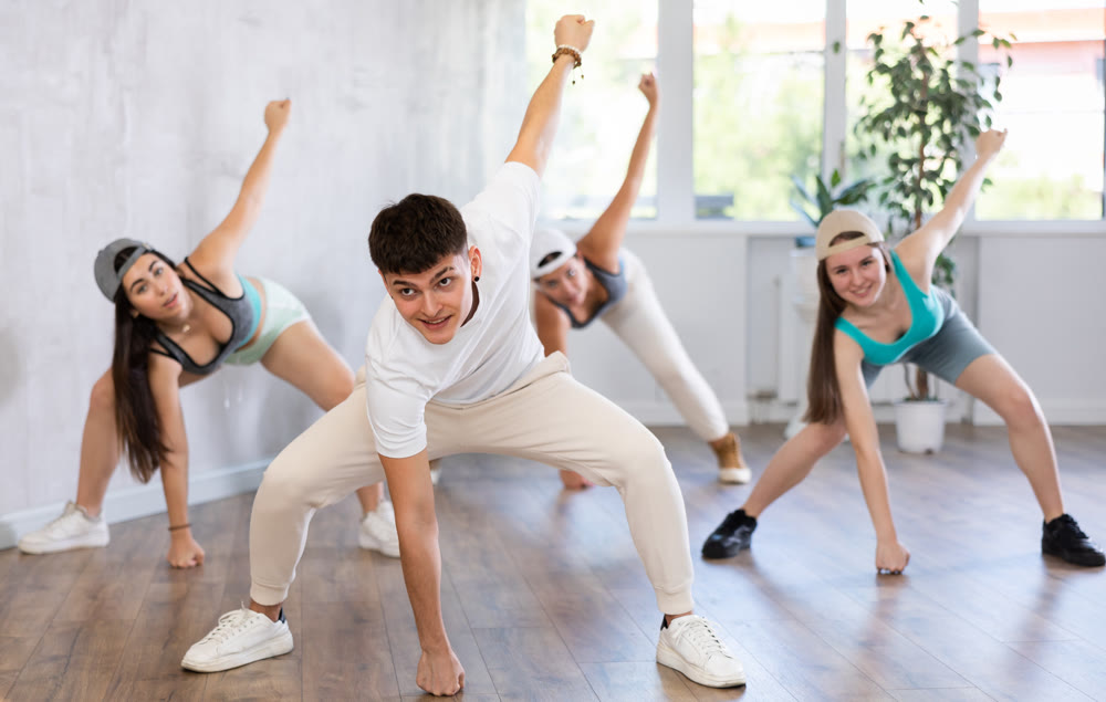 Portrait of positive teenager learning dynamic dance moves with group of teens in studio