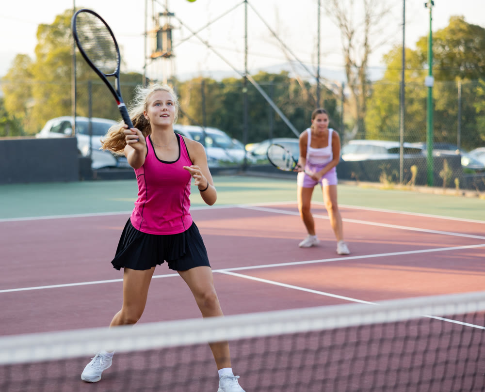Young beautiful girl in pink t-shirt and her female partner playing tennis