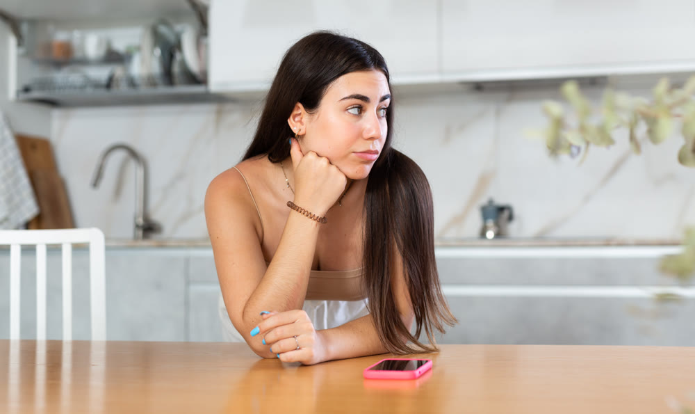 Young woman waiting for message on phone in kitchen