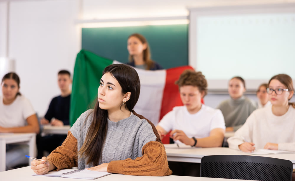 Teacher stands behind students with flag of Italy
