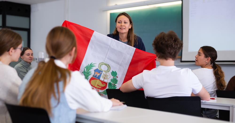 Adult female teacher showing flag of Peru to students