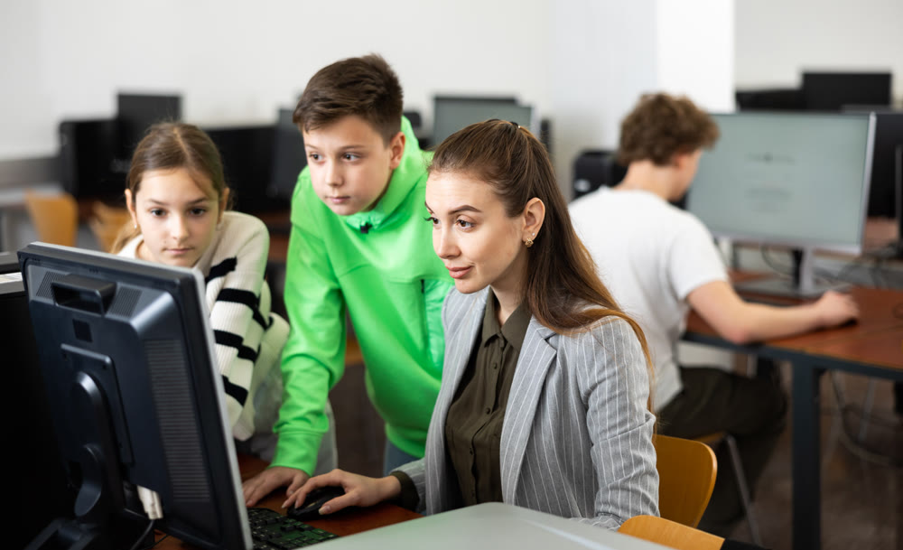 Female teacher helping schoolboy and schoo lgirl in computer class