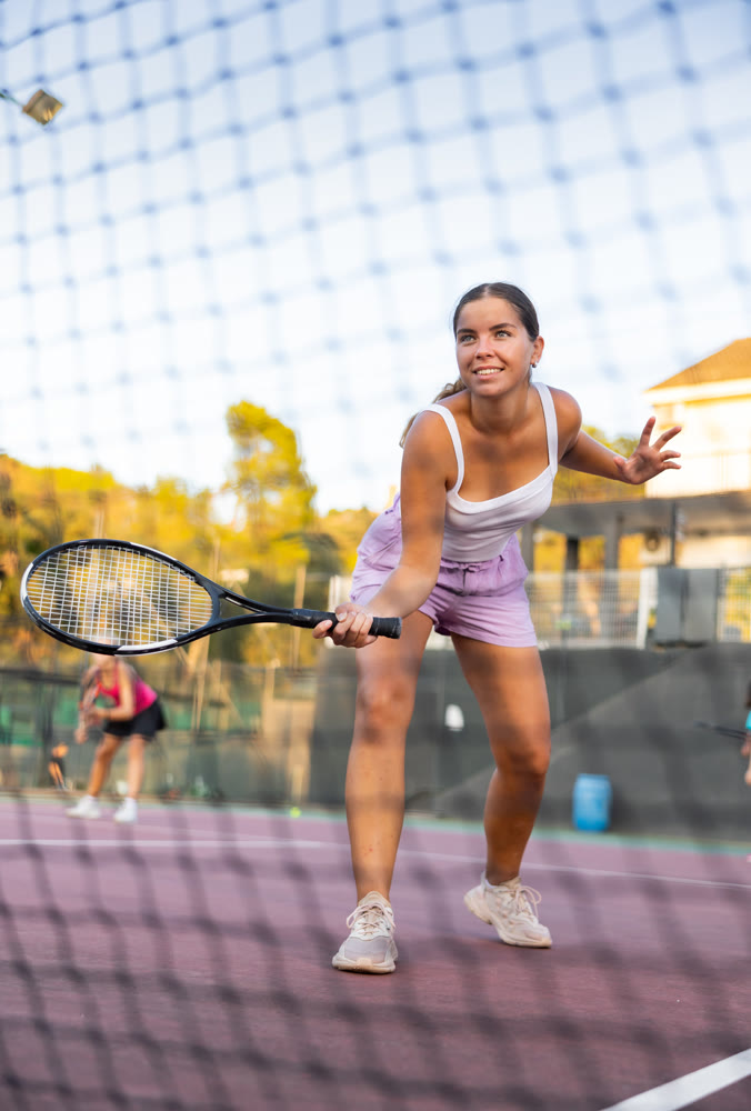 Sporty woman plays tennis on court. View through tennis net