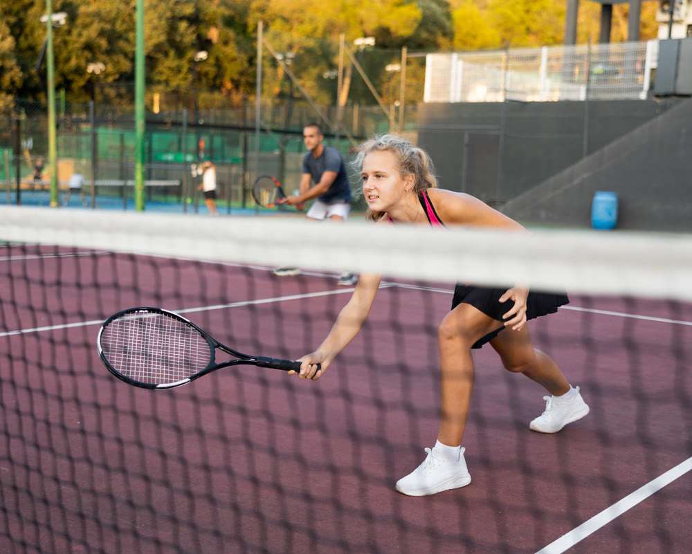 Sporty woman plays tennis on court. View through tennis net