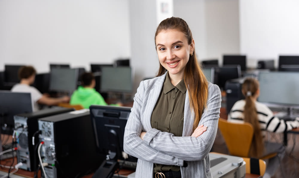 Smiling female teacher of information technology school standing in classroom