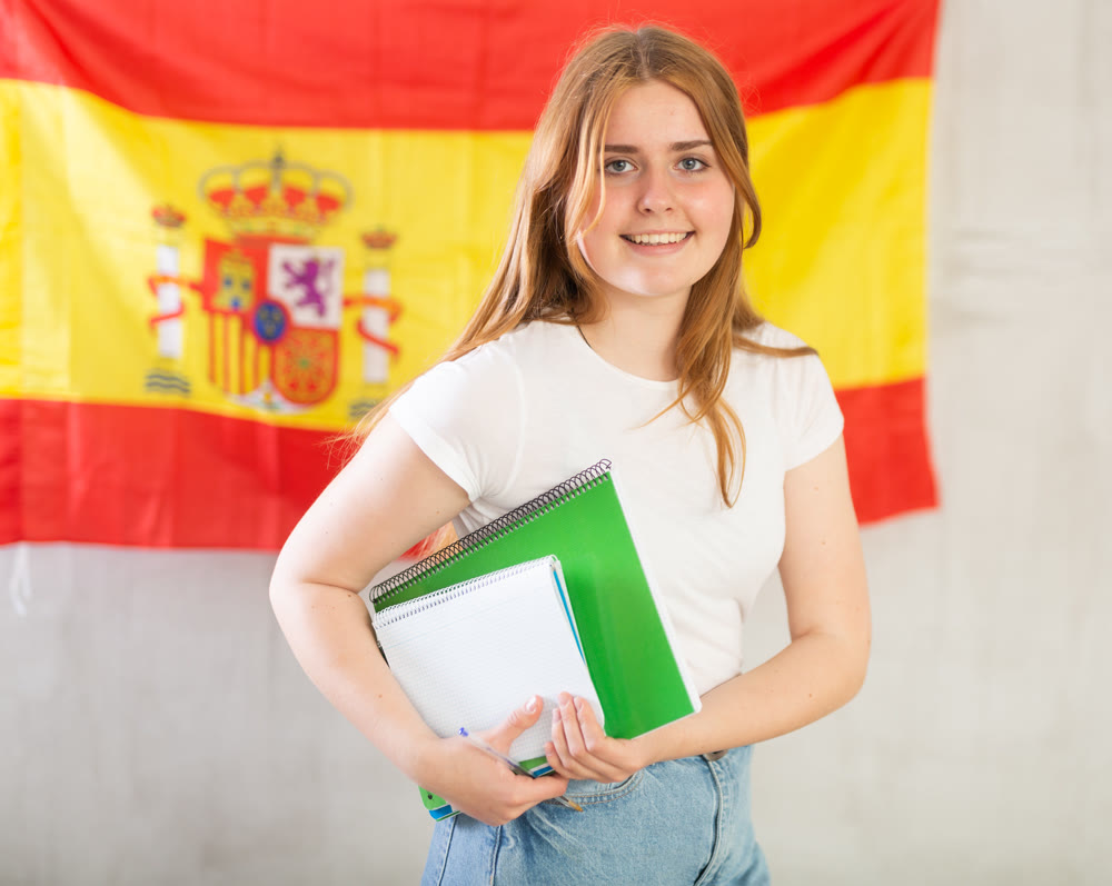 Portrait of a smiling satisfied girl student with notebooks in her hands against the background of flag of Spain