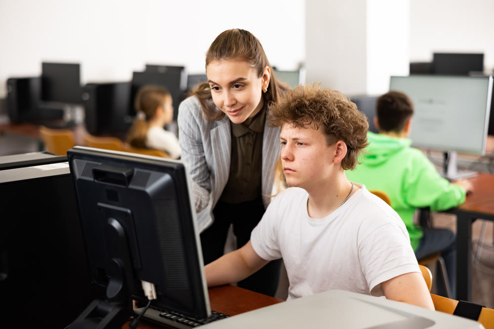 Female teacher helping focused teenage student in computer lab