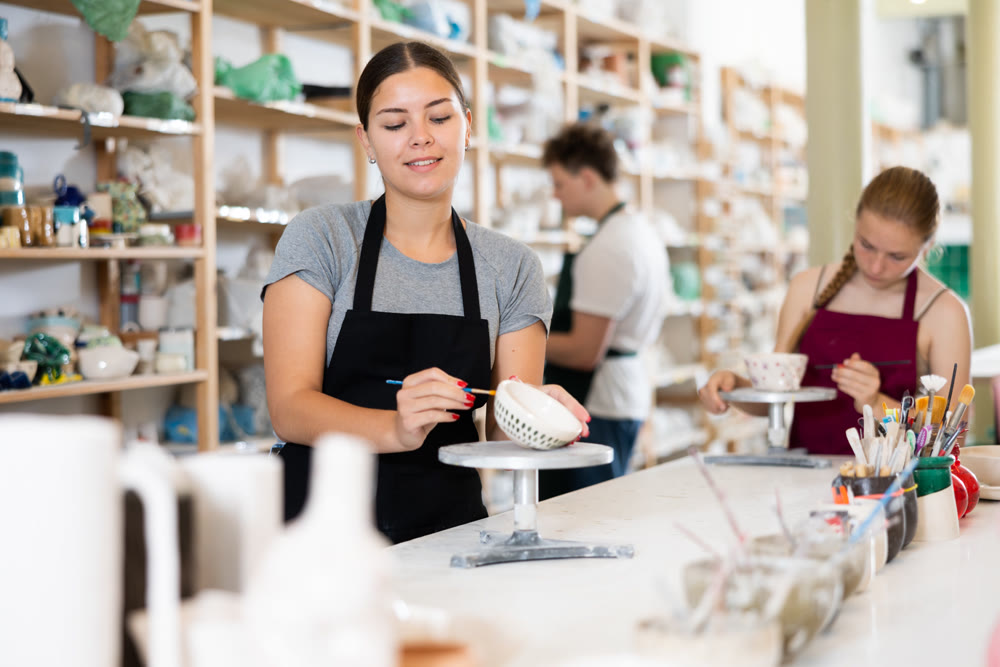 Young woman painting ceramic cup in ceramic workshop