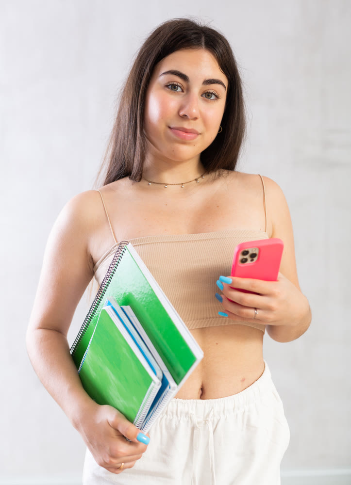 Young woman posing with stack of notebooks and phone in studio