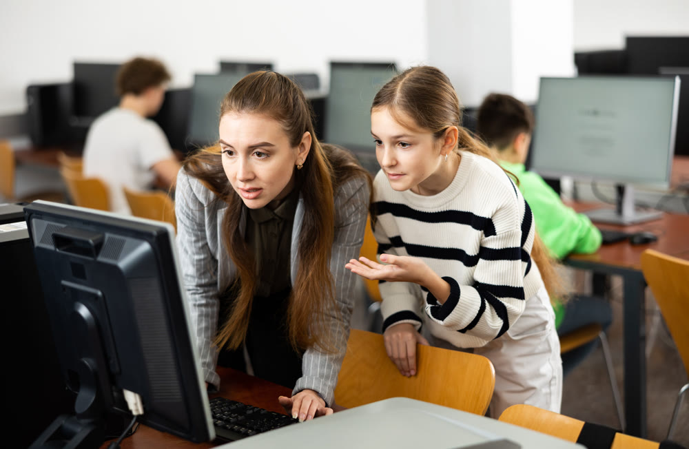 Teacher explaining task solution to pupil during computer science lesson