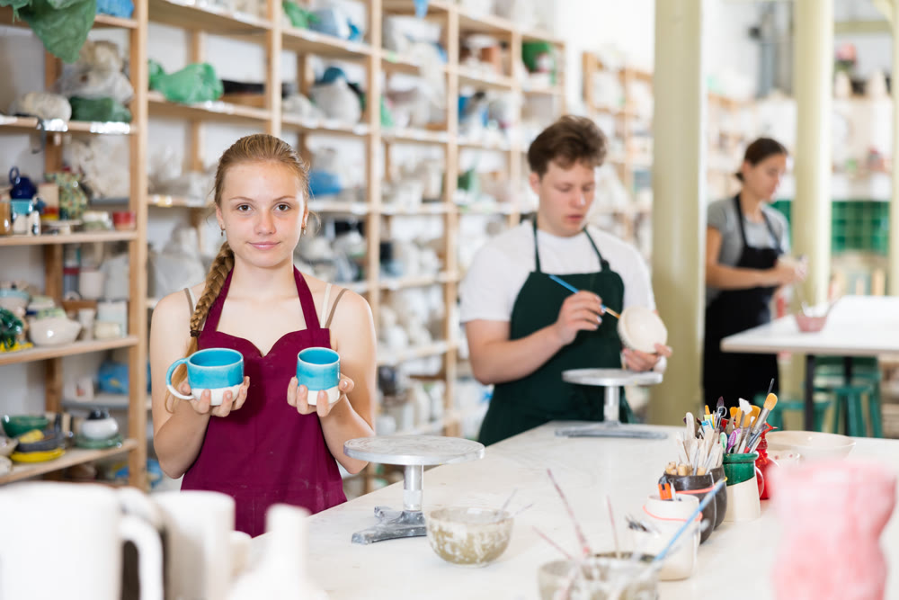 Satisfied teenager girl shows cup created by himself in clay workshop