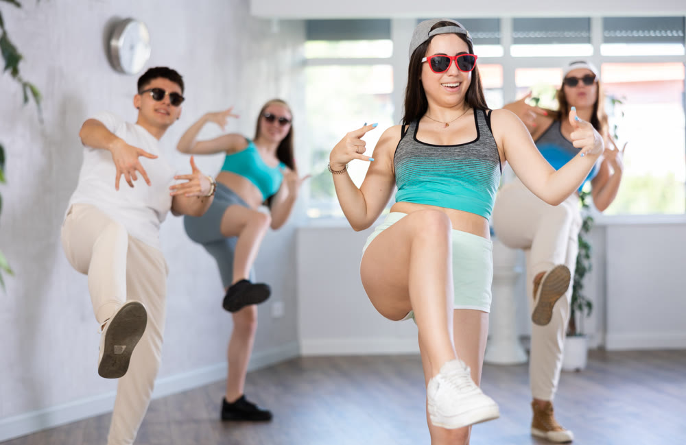 Group of young girls in dark glasses and ball cap and guy dance jazz-funk in fitness club.